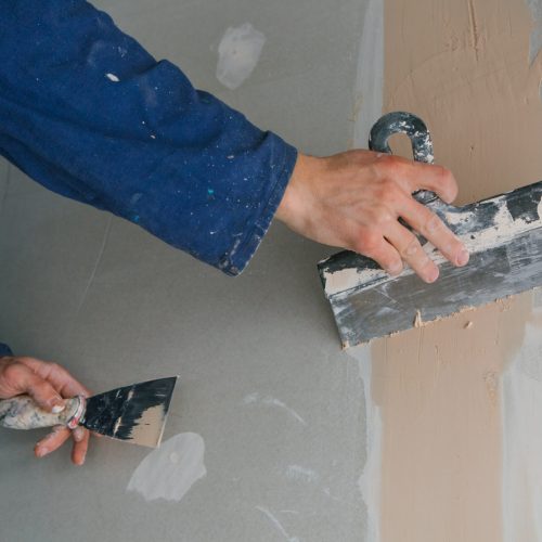 plasterer man works plastering two trowels on plasterboard in blue uniform